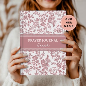 May include: A floral-patterned prayer journal with a white background and pink floral design. The journal has a pink band across the center with the words "PRAYER JOURNAL" and a name. A pink circle with the text "ADD HER NAME" is in the upper right corner.