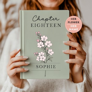May include: A sage green hardcover book featuring the text Chapter EIGHTEEN and the name SOPHIE in black lettering. A central illustration depicts a delicate branch with light pink cherry blossoms and buds. A circular pink badge reads HER FLOWER HER NAME.