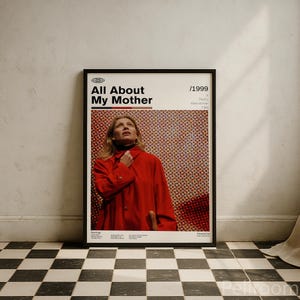 Könnte beinhalten: Ein gerahmtes Filmplakat für "Alles über meine Mutter" (1999) mit einer Frau in einem roten Mantel. Das Plakat hat einen schwarzen Rahmen und steht vor einer weißen Wand und einem schwarz-weiß karierten Boden.
