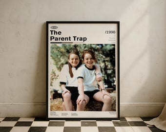 May include: Framed movie poster for "The Parent Trap" (1998). The poster shows two young women in white shirts with black trim and black shorts. The title is in bold white text, with the year 1998 in the upper right corner. The poster is in a black frame.