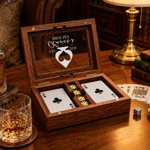 May include: A rectangular wooden box with a hinged glass lid featuring the white text DICE SET, Oliver's, and EST. 2026 above a spade symbol. The interior contains two decks of playing cards and a row of four cream-colored dice with black pips.