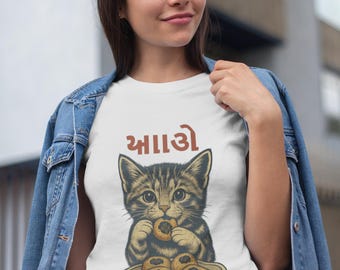 May include: White t-shirt featuring a detailed illustration of a tabby cat eating a pastry from a plate. The shirt has text above the cat. The person in the image is wearing a denim jacket.
