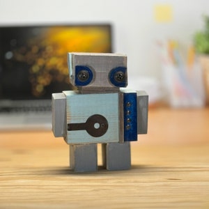 May include: A wooden robot toy with a light blue body, gray legs, and blue accents. The robot has a black and white design on its chest and blue screws for eyes.