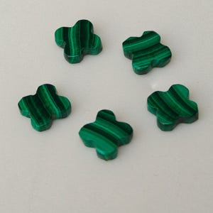 May include: Five green malachite clover-shaped stones. Each stone features a unique pattern of dark and light green stripes. The stones are smooth and polished, with a three-dimensional appearance. The clover design is a classic symbol of luck and nature.