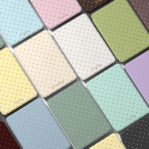 May include: A selection of phone cases in pastel shades, featuring a polka dot design and a name in gold lettering. Colours include blue, pink, yellow, green, and white. The cases are arranged in a grid pattern.