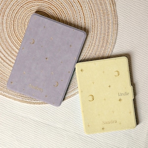 Può includere: Due custodie per e-reader Kindle. Una è lavanda con stelle dorate, lune e il nome "Audrey". L'altra è gialla con stelle dorate, lune, il nome "Sandra" e la parola "Kindle".