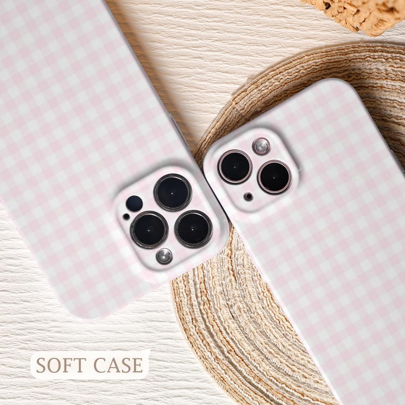 May include: Two phone cases with a pink and white gingham pattern. The cases have a soft case design and are shown on a neutral surface. The cases have multiple camera lenses and a flash. The text "SOFT CASE" is visible.