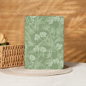 Op de afbeelding: Een saliegroene tablethoes met een wit bloemenpatroon. Het ontwerp bevat gedetailleerde contouren van bloemen, bladeren en stelen. De hoes is rechthoekig en lijkt gemaakt van een glad materiaal. De achtergrond is een houten oppervlak.