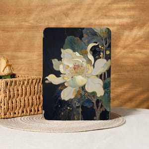以下が含まれることがあります： 花柄のタブレットケース。アートワークは、濃い青色の背景に、黄色と金のアクセントが付いた大きな白い花を特徴としています。緑の葉と金のきらめきが詳細を追加します。ケースは白い表面にあります。