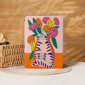 Może przedstawiać: Etui na tablet z fantazyjną ilustracją kota w niebieskie paski, siedzącego przed bukietem kwiatów. Tło to połączenie różu i pomarańczy, z zielonymi liśćmi i kolorowymi kwiatami.