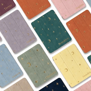 May include: A collection of personalized tablet cases in various colors, including purple, orange, and green. Each case features a gold celestial design of stars and moons, with a name printed in gold lettering.