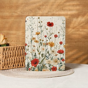 Op de afbeelding: Een tablethoes met een bloemenontwerp, met rode klaprozen, gele en witte madeliefjes en andere wilde bloemen. De hoes heeft een crèmekleurige achtergrond met zwarte spikkels. De bloemen zijn gerangschikt in een veldachtig patroon.