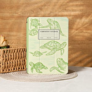 May include: A light green composition notebook cover featuring multiple green line drawings of sea turtles. The text "COMPOSITION NOTEBOOK" is centered on the cover, with additional text below indicating page count and size.
