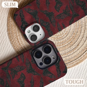 May include: Two phone cases with a dark red background and a pattern of black bats. One case is labeled "SLIM" and the other is labeled "TOUGH". The cases have camera cutouts.