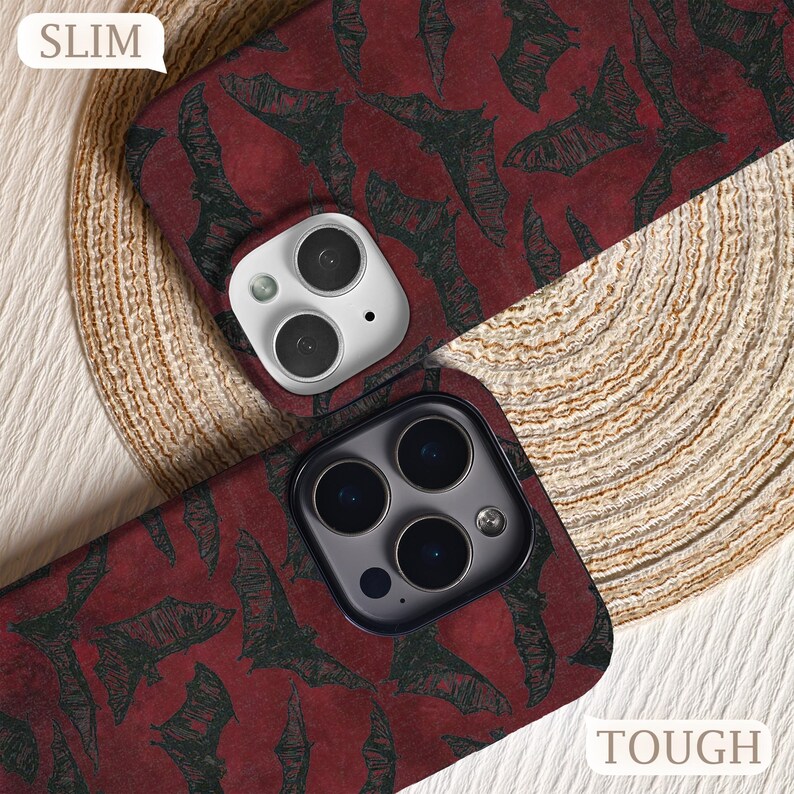 May include: Two phone cases with a dark red background and a pattern of black bats. One case is labeled "SLIM" and the other is labeled "TOUGH". The cases have camera cutouts.