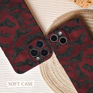 May include: Two phone cases with a repeating pattern of black bats on a deep red background. The cases have camera cutouts and the text "SOFT CASE" is visible at the bottom. The cases are displayed on a woven surface.