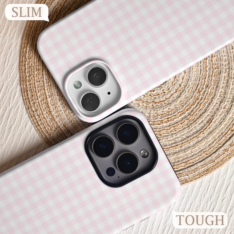 May include: Two phone cases with a pink and white gingham pattern. One case is labeled "SLIM" and the other is labeled "TOUGH". The cases have camera cutouts and are on a textured surface.