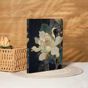 May include: A hardcover journal featuring a large white flower with yellow and gold accents against a dark blue background. The floral design includes green leaves and stems. The journal is displayed on a white surface.