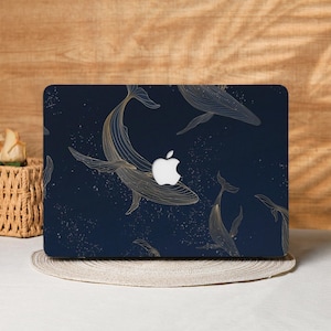 Puede incluir: Funda para portátil azul marino con un diseño de ballenas doradas. Las ballenas están representadas con finas líneas, sobre un fondo de pequeños puntos blancos dispersos. El logotipo de Apple es visible.