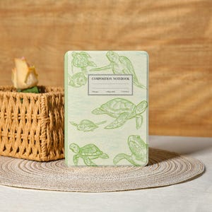 Op de afbeelding: Een compositieboek met een lichtgroene kaft met meerdere groene lijntekeningen van zeeschildpadden. Het notitieboek heeft de woorden "COMPOSITION NOTEBOOK" op de voorkant gedrukt. Het notitieboek is 19 x 23,5 cm.
