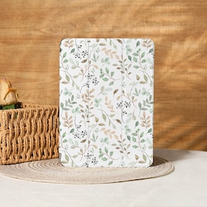 Könnte beinhalten: Eine weiße Tablet-Hülle mit einem Aquarellmuster aus grünen, braunen und beigen Blättern und Beeren. Die Hülle ist vor einem neutralen Hintergrund platziert, was auf ein von der Natur inspiriertes Thema hindeutet. Das Design ist zart und für eine Vielzahl von Geschmäckern geeignet.