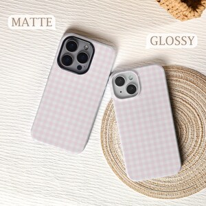 May include: Two phone cases with a pink and white gingham pattern. One case is labeled "MATTE" and the other "GLOSSY". The cases are on a light-colored surface with a woven mat in the background.