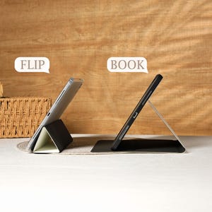 May include: Two tablet cases, one in a "flip" position and the other in a "book" position. The cases are black with a silver stand. The tablet screens are visible. The background is a light brown wooden surface.
