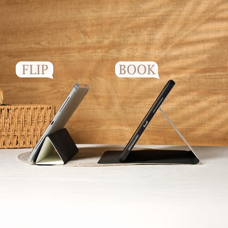May include: Two tablet cases, one in a "flip" position and the other in a "book" position. The cases are black with a silver stand. The tablet screens are visible. The background is a light brown wooden surface.