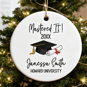May include: White ceramic graduation ornament with the text "Mastered It!" and "20XX". Features a black graduation cap with a gold tassel and a rolled diploma. Includes the name "Janessa Smith" and "Howard University".