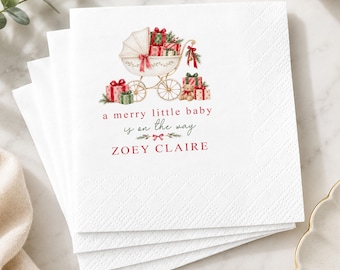May include: A stack of white paper napkins featuring a printed illustration of a vintage baby carriage filled with wrapped Christmas gifts and a teddy bear. The text reads a merry little baby is on the way and the name ZOEY CLAIRE in red.