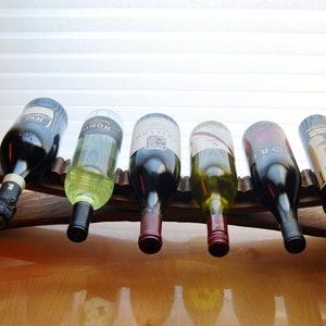 May include: A wooden wine rack with six bottles of wine. The rack is made of dark wood and has a rustic look. The bottles are all different colors and have different labels.