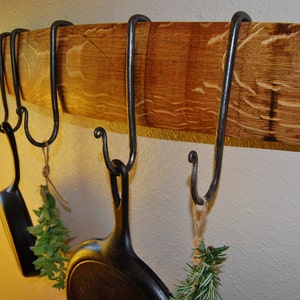 May include: A reclaimed wood shelf with five hand-forged iron hooks, perfect for hanging kitchen utensils or other items. The shelf is stained a rich brown color and has a rustic look.