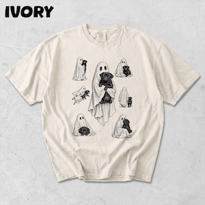 Puede incluir: Una camiseta de manga corta color marfil con un estampado gráfico en tinta negra de varios fantasmas sosteniendo carlinos negros. La palabra IVORY está impresa en la esquina superior izquierda. El diseño incluye ilustraciones de fantasmas con sábanas blancas.
