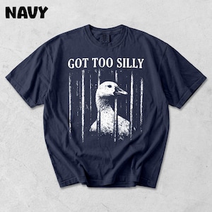 Op de afbeelding: Marineblauw t-shirt met een witte afbeelding van een gans achter tralies en de tekst "GOT TOO SILLY". Het woord "NAVY" staat linksboven in het wit gedrukt. Het shirt is gemaakt van een zacht materiaal.