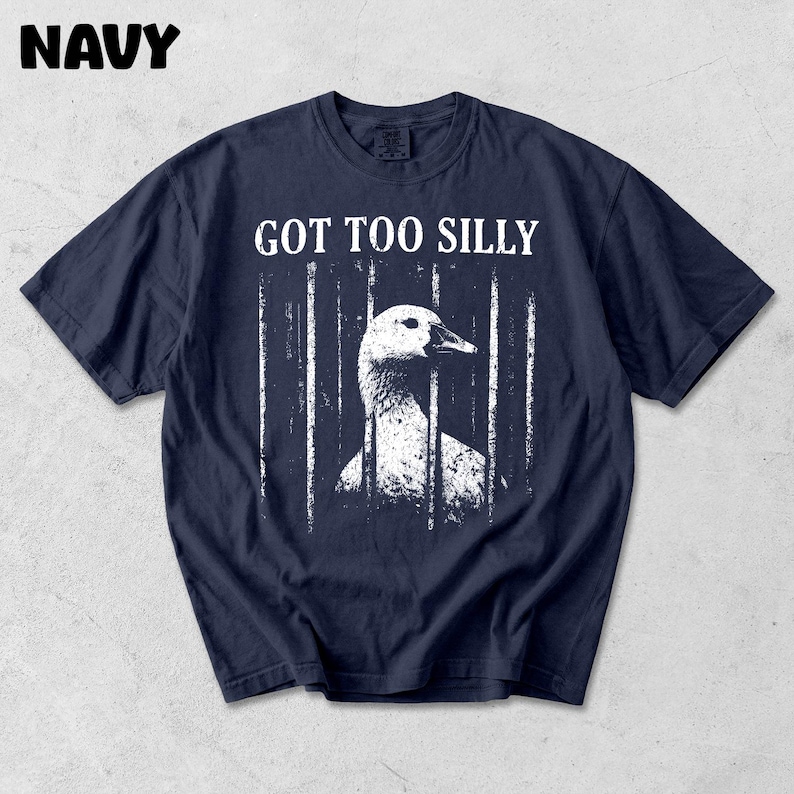 Op de afbeelding: Marineblauw t-shirt met een witte afbeelding van een gans achter tralies en de tekst "GOT TOO SILLY". Het woord "NAVY" staat linksboven in het wit gedrukt. Het shirt is gemaakt van een zacht materiaal.