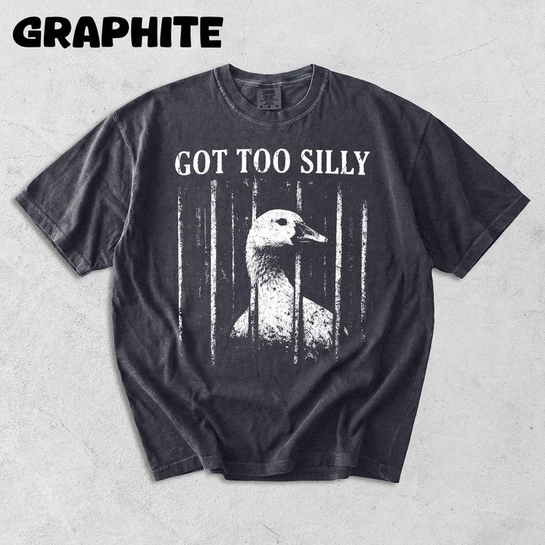 Op de afbeelding: Grafietkleurig t-shirt met de tekst "GOT TOO SILLY" boven een witte illustratie van een gans achter tralies. Het shirt heeft een vintage, versleten uitstraling.