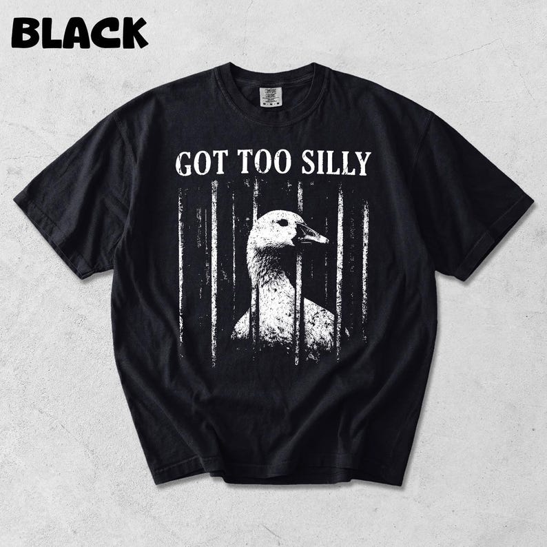 Op de afbeelding: Zwart t-shirt met de tekst "GOT TOO SILLY" boven een wit en grijze illustratie van een gans achter tralies. Het woord "BLACK" staat in de linkerbovenhoek van het shirt.