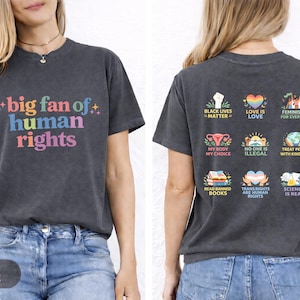 Puede incluir: Camiseta gris oscuro con el texto "big fan of human rights" en letras coloridas. La parte posterior de la camiseta presenta varios iconos gráficos con frases como "Black Lives Matter" y "Love is Love".