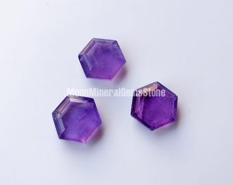 Könnte beinhalten: Drei sechseckige Amethyst-Edelsteine mit facettierten Kanten werden vor einem weißen Hintergrund gezeigt. Die Edelsteine haben eine tiefviolette Farbe mit Farbvariationen. Das Bild ist gut beleuchtet und hebt die Facetten und die Farbe der Steine hervor.