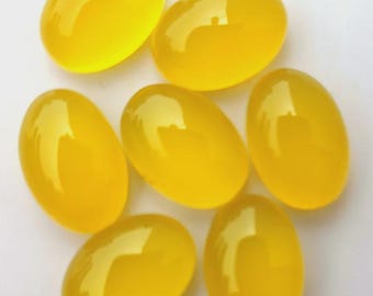 May include: Seven polished, oval-shaped yellow gemstones. The gems have a smooth, glossy surface, reflecting light. The stones are arranged in a scattered pattern, showcasing their vibrant color and shape. These gemstones are suitable for jewelry making.