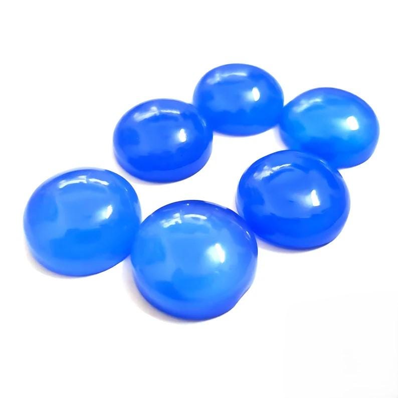 Puede incluir: Siete gemas cabuj&oacute;n azules brillantes dispuestas en un patr&oacute;n circular. Cada piedra tiene una superficie lisa y redondeada y un color vibrante y saturado. Las gemas est&aacute;n sobre un fondo blanco.