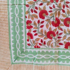 Puede incluir: Un tejido con un centro blanco con un patrón floral rojo y hojas verdes. El borde consiste en una banda verde con un diseño de eslabones blancos y un borde dentado, enmarcado por un borde exterior de finas rayas verticales amarillas y blancas.