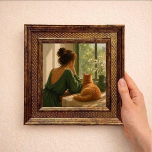 Op de afbeelding: Een vierkant wandkunstwerk met een schilderij van een persoon in een groene jurk die naast een oranje kat bij een raam met witte bloemen in een vaas zit. Het kunstwerk is gevat in een donkere, getextureerde, goudkleurige houten lijst.