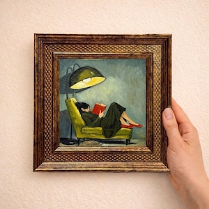 Op de afbeelding: Een ingelijst schilderij toont een persoon in donkere kleding zittend op een limoengroene fauteuil, lezend in een rood boek onder een grote zwarte vloerlamp. Het kunstwerk zit in een getextureerde, donkergouden lijst met een ruitpatroon.