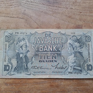 Op de afbeelding: Een vintage tien Gulden bankbiljet van De Javasche Bank, met portretten van figuren in traditionele kledij. De biljet is gedateerd 6 januari 1938 en bevat Nederlandse tekst. Het bankbiljet is rechthoekig en heeft een lichtblauwe en grijze kleurstelling.