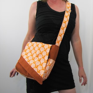 May include: A messenger bag with a flap closure and adjustable strap. The bag features a repeating white leaf pattern on an orange background. The trim and strap are a solid brown color.