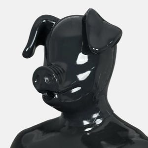 Op de afbeelding: Een glanzend zwart masker voor het hele hoofd in de vorm van een varken, met opvallende oren, een snuit met twee neusgaten en een ronde opening bij de mond. Het oppervlak is glad en reflecterend en bedekt het hoofd en de nek.