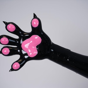 以下が含まれることがあります： ピンク色のパッドと爪が付いた黒い足。足には5本の指があり、ピンク色のパッドと鋭い黒い爪が付いています。足は光沢があり、滑らかな素材でできているようです。