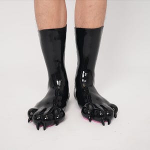 以下が含まれることがあります： 黒く光沢のある、膝丈のブーツ。爪の形をしたつま先とピンク色のソールが特徴です。ブーツは光沢のある仕上がりで、動物の足に似せてデザインされています。