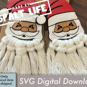 May include: Two Santa Claus ornaments with red hats and macrame beards. The Santa faces are painted with brown skin, white beards, and black accents. The text "MADE BY SPALT LIFE HANOVER CO, VA" is visible. The image also includes the text "SVG Digital Download".